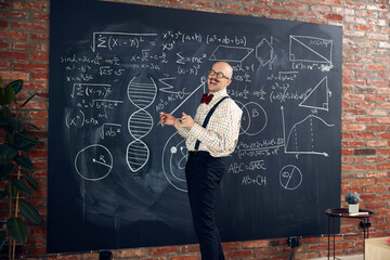 Young man, scientist, lecturer standing by blackboard with math and scientific formulas, making...