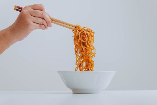 Hand takes fried Indonesian instant noodles or Indomie using wooden chopsticks for food. Modern and fast food. Isolated white background.
