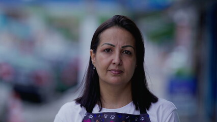 Portrait of a Brazilian woman with serious expression standing in street looking at camera. Female person wearing apron worker face close-up