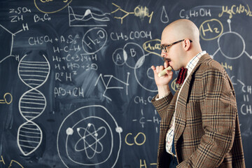 Young man, scientist standing by blackboard with formulas and calculations. Chemistry lessons. Concept of education, science, profession and occupation, knowledge - obrazy, fototapety, plakaty