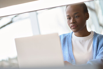 Busy African Black girl student using laptop computer technology sitting at desk. Serious young woman elearning or hybrid working looking at pc, watching webinar, searching job online. Copy space.