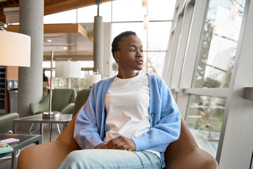 Pensive African Black teenage girl university or college student refugee sitting in chair in...