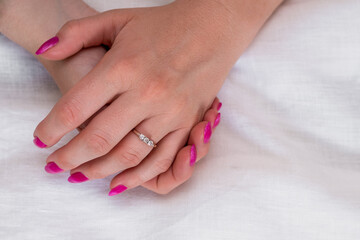 Close-up of well-groomed female pink nails. Beautiful clear fingers of a young girl with nice manicure and Glitter Nail Polish. Girl hands on a white background. Girl is wearing two diamond rings.