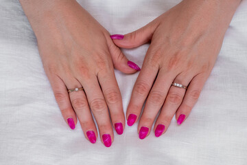 Naklejka premium Close-up of well-groomed female pink nails. Beautiful clear fingers of a young girl with nice manicure and Glitter Nail Polish. Girl hands on a white background. Girl is wearing two diamond rings.