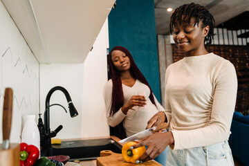 Black lesbian couple smiling while cooking together in kitchen