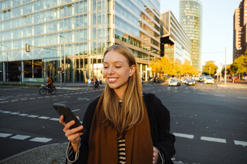 Smiling woman reading message on her smartphone while standing at street