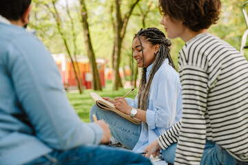 Young smiling woman drawing while sitting with friends in park