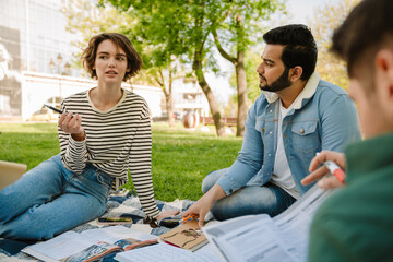 Group of students friends doing homework while sitting in park