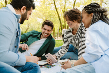 Group of smiling students using smartphone while spending time together in park
