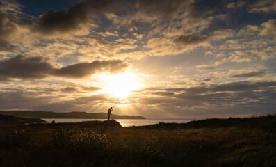 Fototapeta premium View of the coast at sunset over the Cantabrian Sea with the sun in front and the silhouette of a fisherman.