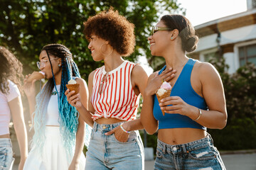 Group of cheery women eating ice cream while spending time together outdoors