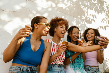 Group of cheery women eating ice cream and taking selfie while spending time together outdoors