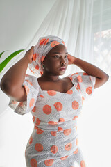 Stylish ethnic woman in dress standing near window