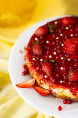 Homemade cheesecake with red berries topping on yellow table cloth on laid table