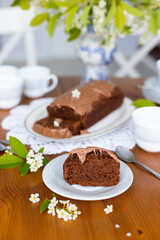 Homemade chocolate cake with chocolate glaze on white plate on laid table with bouquet of spring blossom apple tree branches