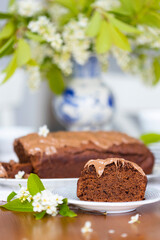 Homemade chocolate cake with chocolate glaze on white plate on laid table with bouquet of spring blossom apple tree branches