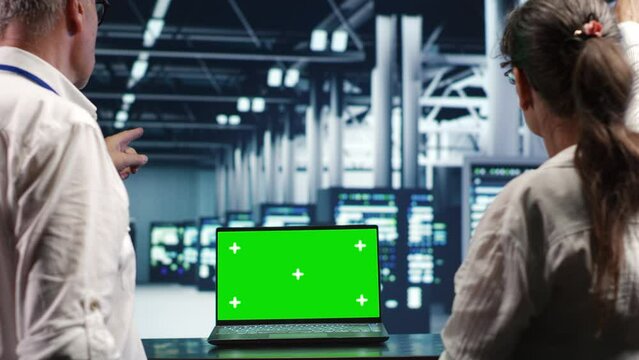 Trained computer scientists looking around high tech data center, using mockup laptop to crosscheck disaster recovery plan and assess server systems in need of replacement, preventing collapse