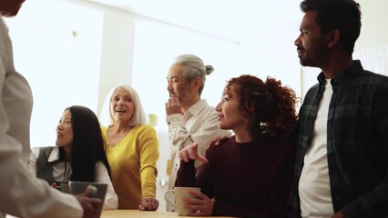 Happy multiethnic people drinking tea during lunch break at work - Group of multi-generational friends having fun laughing together - Soft focus on Asian senior man face