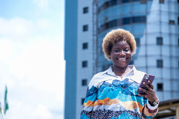 African woman standing in front of a tall building holding a cell phone