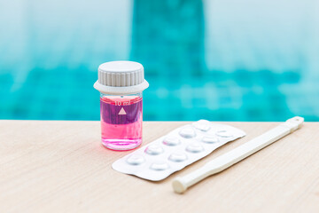 Pool water in glass vials with pH table reagents and stirring rod on swimming pool edge, water...