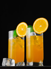 Two glasses of orange cocktail with ice cubes and mint leaves on a dark background. Vertical frame. Low angle view.