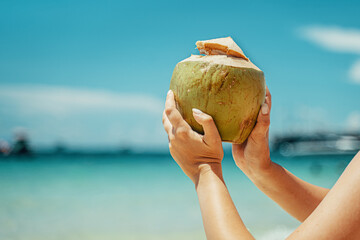 A woman holds a coconut on the background of the sea. Coconut cocktail on the beach. Azure sea