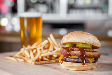 Hamburger with onion ring, french fries and tab beer. Plated tastefully in a bar setting