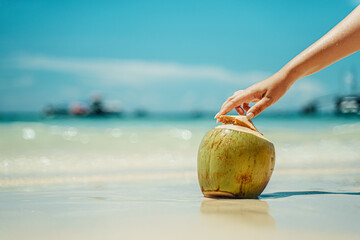Young woman opens a coconut. Coconut on the beach. Blue sea