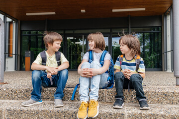 Children sit on the steps of the school and talk. Schoolchildren rest during recess or after school and communicate with each other.