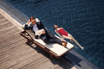 Business clothes, reading newspaper. Man with woman is in the pool together