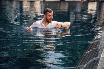 Checking the time, in the water. Handsome man in formal clothes is in the pool