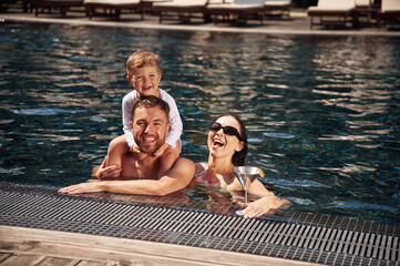 Smiling, having fun. Happy family of father, mother and son are in the pool