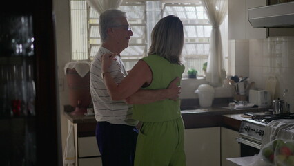 Candid happy senior couple dancing in kitchen. Joyful middle-age man and woman engaged in rhythmic dance