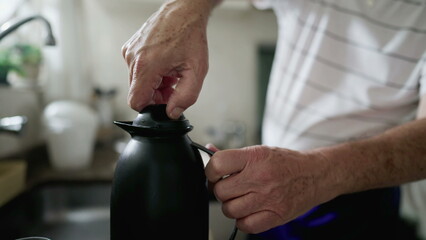 Close-up hand tightening and loosening thermos bottle preparing warm drink, coffee or tea - obrazy, fototapety, plakaty