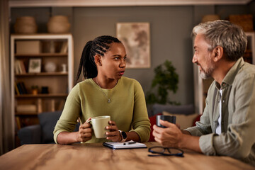Diverse couple having a conversation while sitting at a table at home.