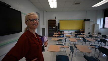 Portrait of smiling happy teacher entering an empty classroom, turning lights, on optimistic about the future of education. US American flag and smart board in room.