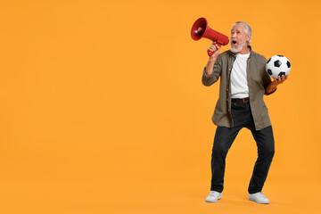 Emotional senior sports fan with soccer ball using megaphone on yellow background, space for text