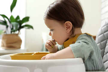 Cute little baby eating healthy food in high chair indoors
