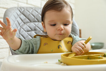 Cute little baby eating healthy food in high chair indoors