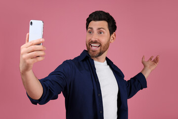 Obraz na płótnie Canvas Smiling man taking selfie with smartphone on pink background
