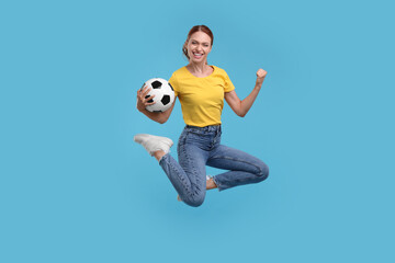 Fototapeta na wymiar Happy fan with football ball jumping on light blue background