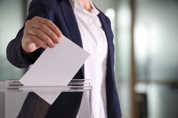 Woman putting her vote into ballot box on blurred background, closeup