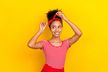 Photo of dreamy pretty girl dressed red striped t-shirt tying hairband looking empty space isolated yellow color background