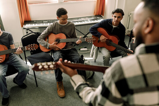 Male teenage students leaning guitar in music class at high school