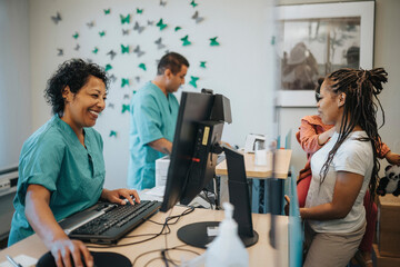 Happy female receptionist talking with mother carrying daughter at receptionist desk in hospital