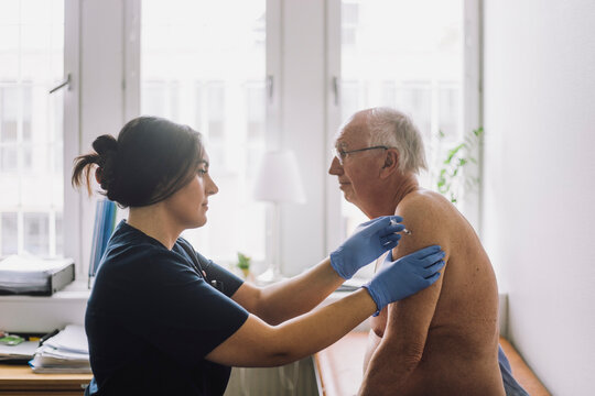 Female nurse giving vaccination to shirtless senior patient at hospital - Powered by Adobe