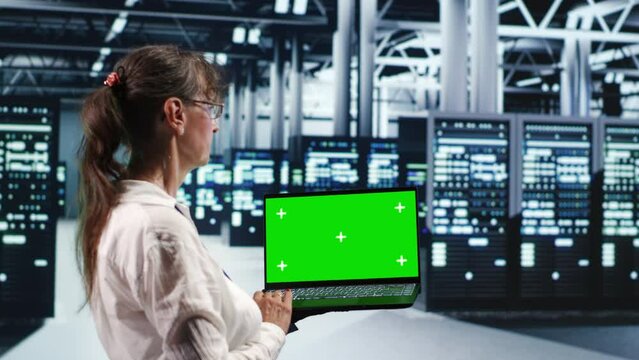 Senior engineer in server room housing high end processors capable of quickly and efficiently performing complex computations and data analysis, using mockup laptop to repair malfunctions