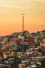 Colorful houses in La Pena district,  Guayaquil, Ecuador, with a beautiful orange sunset and a airplane flying over Transmission tower