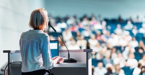 Female speaker giving a talk on corporate business conference. Unrecognizable people in audience at conference hall. Business and Entrepreneurship event - 634731980