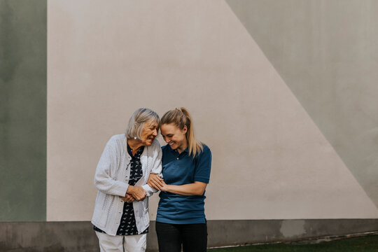Smiling female caregiver standing with senior woman against wall